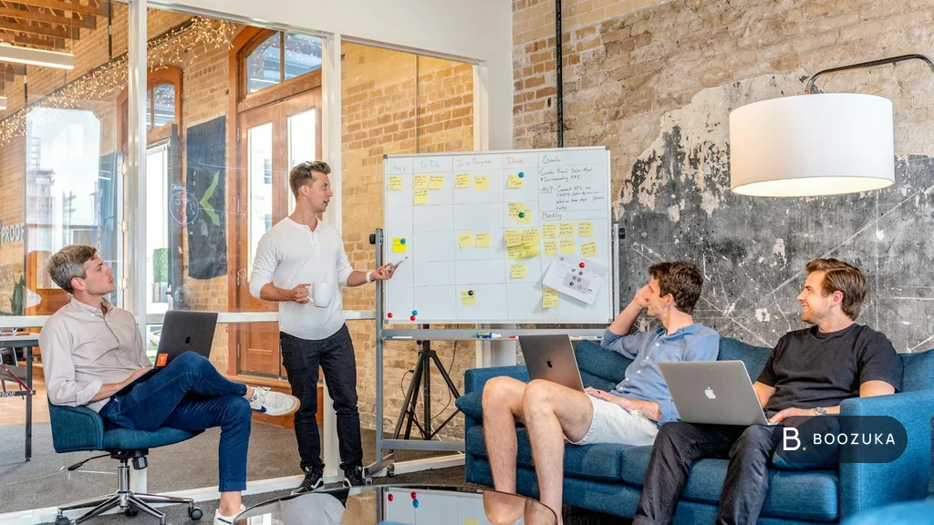 A small team meeting around laptops in a bright office, discussing a marketing plan